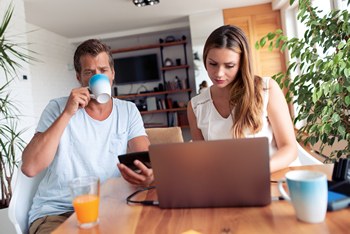 A man and woman collaborate at a table, using a laptop and sipping coffee during their discussion.