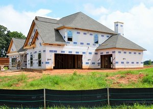 A rural house under construction, featuring wooden beams and scaffolding against a backdrop of trees and open fields.